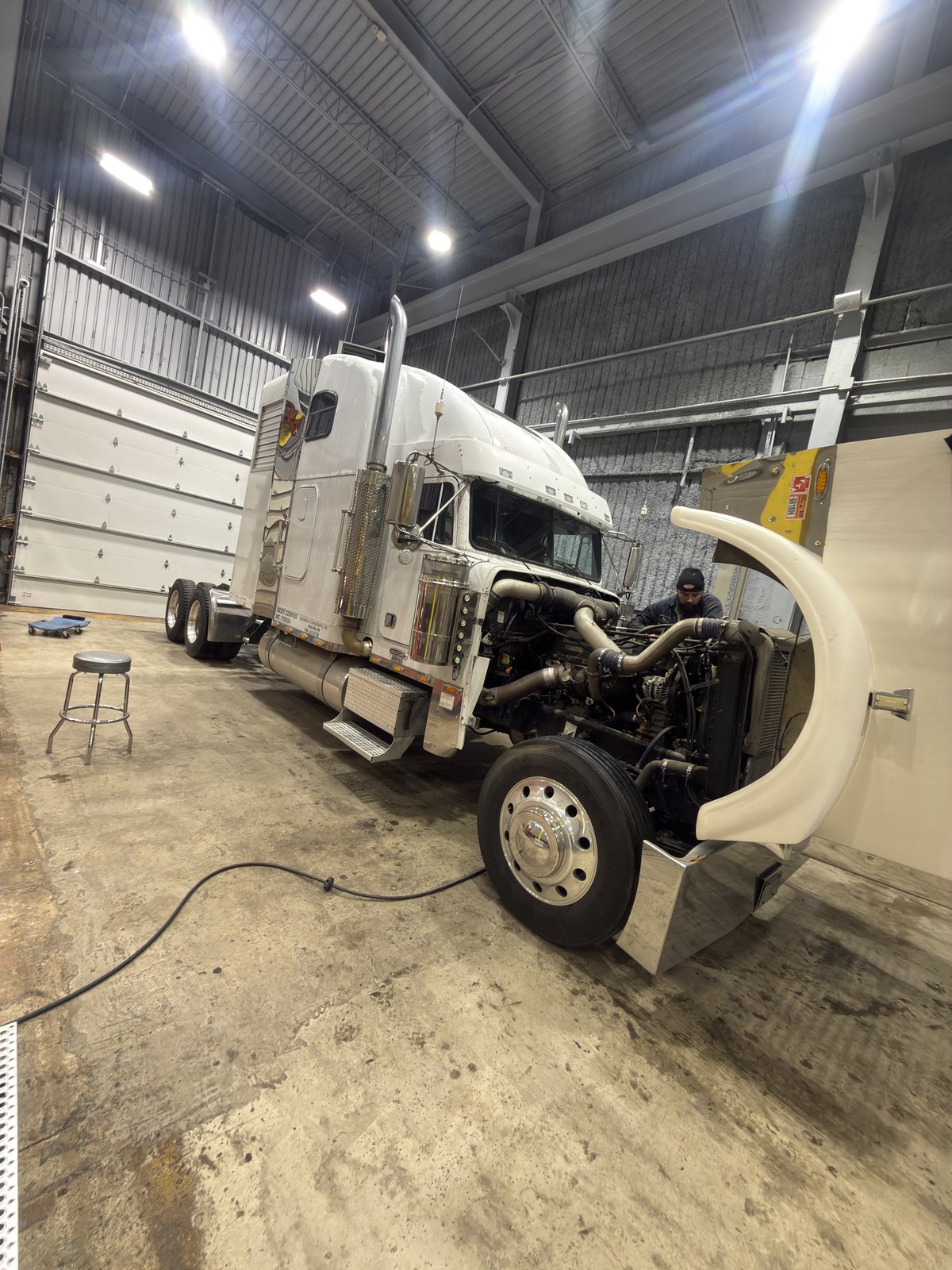 FleetFix technician working under the open hood of a white semi truck